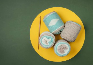 Pastel renklerin yün derileri, yeşil arka planda sarı halkalı ahşap örgü kancası. Üst Manzara. Minimalizm