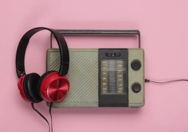 Retro radyo alıcısı, pembe pastel arka planda eski moda kulaklıklar. Eski kitle iletişim araçları Üst görünüm
