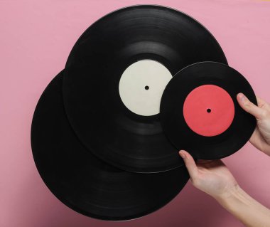 Kadın eli, pembe pastel arka planda vinil plak tutuyor. Üst görünüm