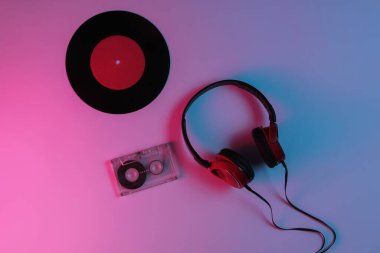 Kablolu kulaklıklar, vinil kayıt, neon mavi-kırmızı renkli ses kaseti. Retro dalga, 80 'lerin popüler kültürü. Üst görünüm