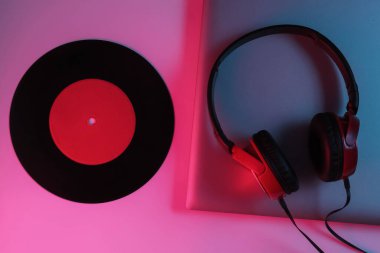 Kulaklıklı ve plaklı bir Lptop. Neon mavi-kırmızı eğimli ışık. Retro dalga, popüler kültür, DJ ekipmanları. Üst görünüm