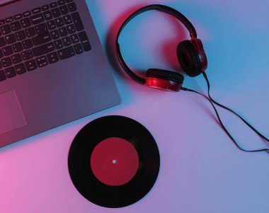 Kulaklıklı ve plaklı bir Lptop. Neon mavi-kırmızı eğimli ışık. Retro dalga, popüler kültür, DJ ekipmanları. Üst görünüm