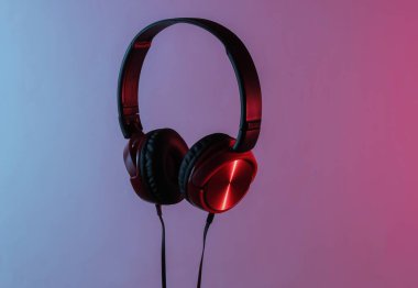 Kablolu yeni kulaklıklar. Kulaklıkların minimalist fotoğrafı. Siyah kırmızı DJ kulaklıklar. Neon mavi-kırmızı eğimli ışık. Retro dalga, 80 'lerin popüler kültürü