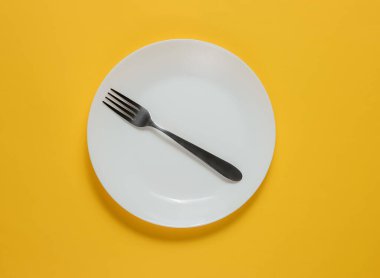 Sarı arka planda çatalı olan boş bir tabak. Stüdyo çekimi. Restoran yemekleri konsepti..