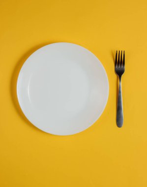 Sarı arka planda çatalı olan boş bir tabak. Stüdyo çekimi. Restoran yemekleri konsepti..