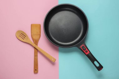 Üzerinde mavi-pembe pastel arka planda spatula pişirilmiş yapışmaz tava. Minimalizm kavramı pişirmek. Üst görünüm