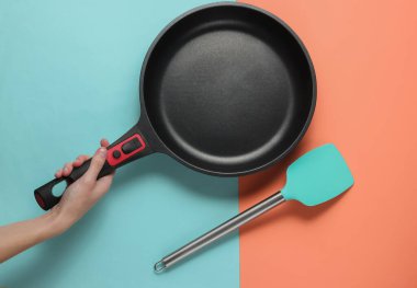 Kadın eli, pembe mavi arka planda çubuksuz tava ve spatula pişiriyor. Üst görünüm