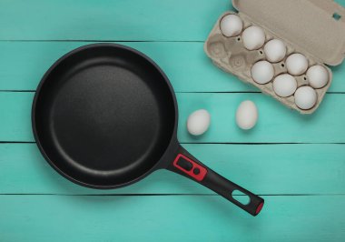 Çubuksuz tava ve mavi ahşap arka planda yumurta tepsisi. Üst görünüm