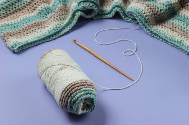 İplikli yün iplikler ve mor arka planda ahşap örgü kancası. Hobiler