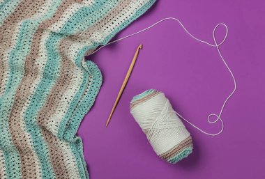 İplikli yün iplikler ve mor arka planda ahşap örgü kancası. Hobiler