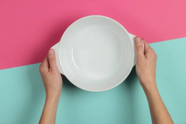 Kadın elleri boş seramik kaseyi pembe mavi arka planda tutar. Üst görünüm