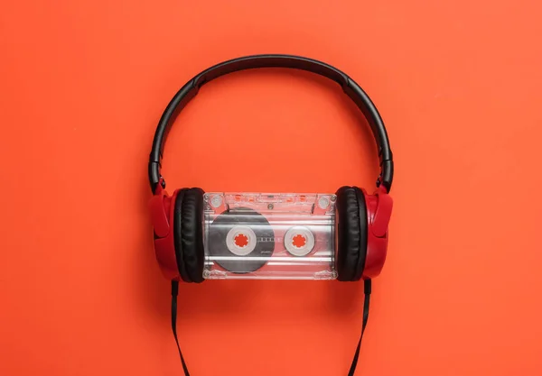 Wired headphones with audio cassette on orange background. Retro style, DJ. Top view, minimalistic music concept.