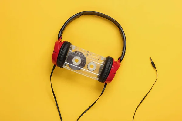 Wired headphones with audio cassette on yellow background. Retro style, DJ. Top view, minimalistic music concept.