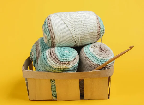 Pastel renklerin yün iplikleri ve sarı arka plandaki sepetin içine tığ işi kanca. Ev Kadınları Hobileri