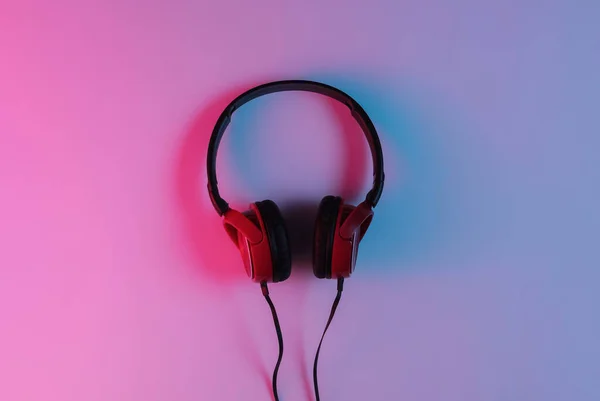 Wired headphones with neon blue-red gradient light. Retro wave, 80s pop culture. Top view