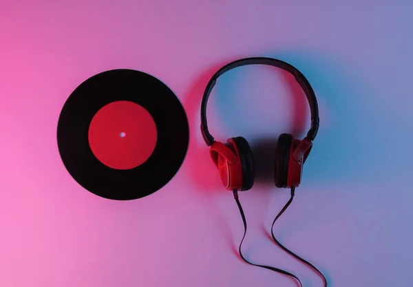 Wired headphones and vinyl record with neon blue-red gradient light. Retro wave, 80s pop culture. Top view