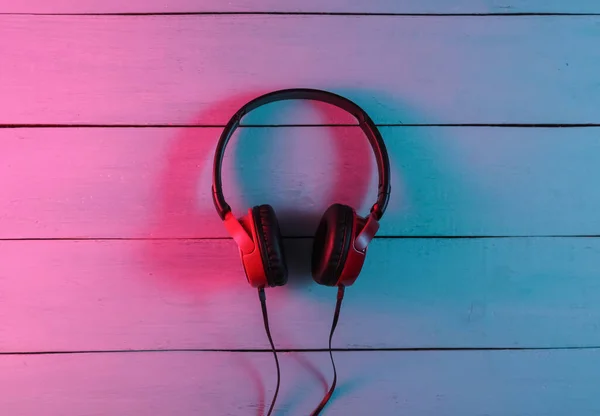 Wired headphones on wooden background. Neon blue-red gradient light. Retro wave, 80s pop culture. Top view