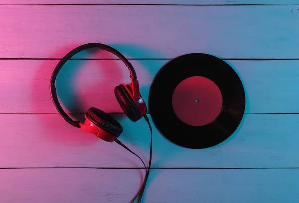Wired headphones and vinyl record on wooden background. Neon blue-red gradient light. Retro wave, 80s pop culture. Top view