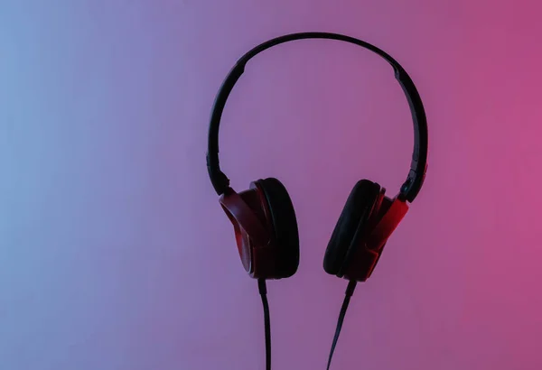 New headphones with cable. Minimalist photo of earphones . Black red dj headphones. Neon blue-red gradient light. Retro wave, 80s pop culture