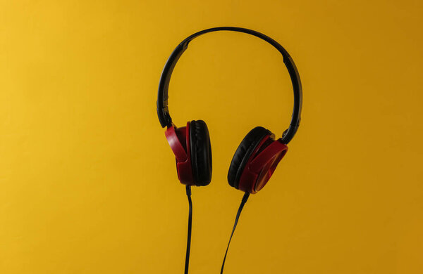 Новые наушники с кабелем. Минималистская фотография наушников на жёлтом фоне. Черные красные наушники диджея