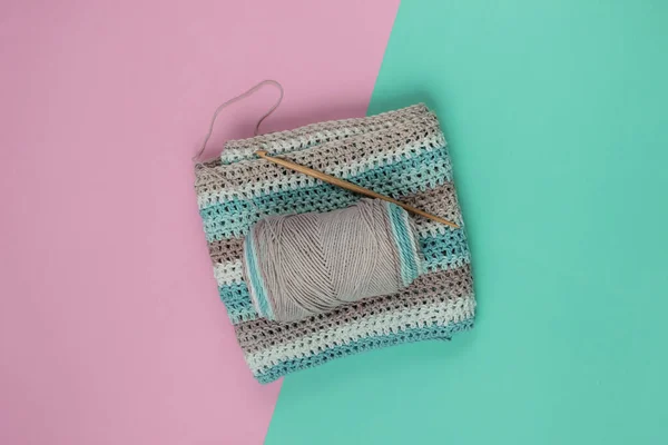 Yarn with skeins of woolen threads and a wooden crochet for knitting on a blue-pink pastel background. Top view