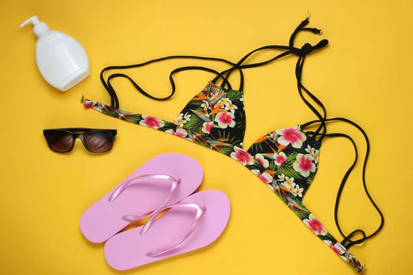 Yaz tatili kavramı. Kadın bikinisi, parmak arası terlik ve sarı arka planda plaj aksesuarları. Kadın mayosunun yukarıdan görünüşü. Düz yatış, üst görünüm. 