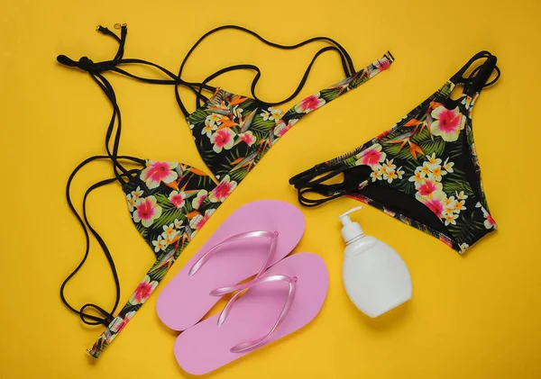 Yaz tatili kavramı. Kadın mayosu, parmak arası terlik ve sarı arka planda plaj aksesuarları. Kadın mayosunun yukarıdan görünüşü. Düz yatış, üst görünüm. 
