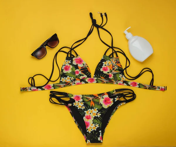 Yaz tatili kavramı. Sarı arka planda kadın mayoları ve plaj aksesuarları. Kadın mayosunun yukarıdan görünüşü. Düz yatış, üst görünüm. 
