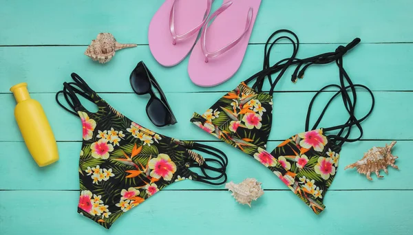 Summer fun background. Woman's swimsuit and beach accessories on blue wooden background. Overhead view of woman's swimwear. Vacation on the beach. Flat lay, top view.