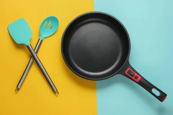 Non-stick pan with cooking spatula on blue yellow background. Cooking minimalism concept. Studio shot. Top view