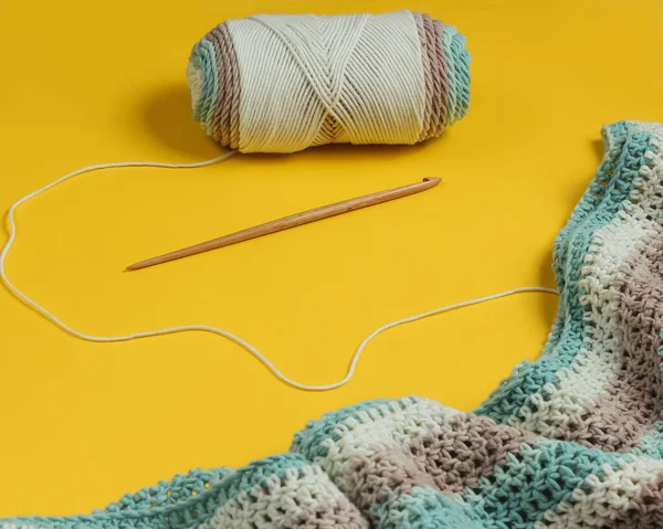 Sarı arka planda yün iplikler ve ahşap örgü kancası. Hobiler