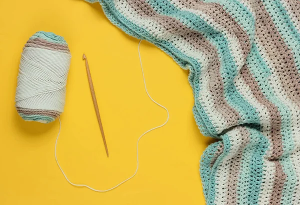 Sarı arka planda yün iplikler ve ahşap örgü kancası. Hobiler
