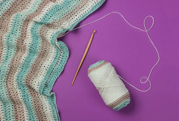 İplikli yün iplikler ve mor arka planda ahşap örgü kancası. Hobiler
