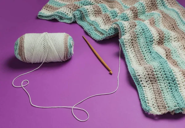 İplikli yün iplikler ve mor arka planda ahşap örgü kancası. Hobiler
