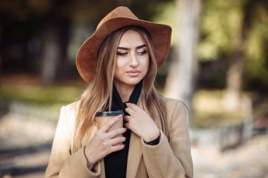 Ceket giymiş ve şapkalı çekici bir kadının portresi. Sonbahar şehir parkında yürü