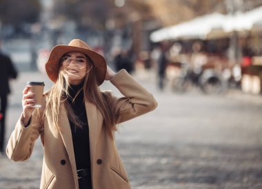 Palto giymiş genç ve şık bir kadın ve şehirde dolaşan bir şapka hissetti ve giderken kahve içti. Sonbahar zamanı