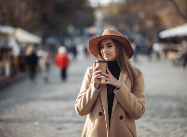 Palto giymiş genç ve şık bir kadın ve şehirde dolaşan bir şapka hissetti ve giderken kahve içti. Sonbahar zamanı