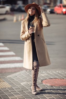 Palto giymiş genç ve şık bir kadın ve şehirde dolaşan bir şapka hissetti ve giderken kahve içti. Sonbahar zamanı