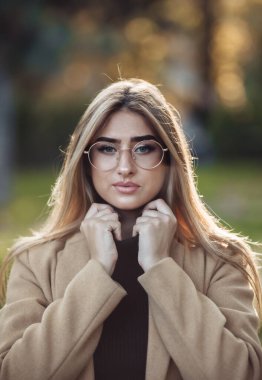 Sonbahar portresi. Parkta gözlüklü ve ceketli neşeli şık bir kadın.