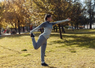 Genç sporcu kadın sonbahar parkında yoga yapıyor.