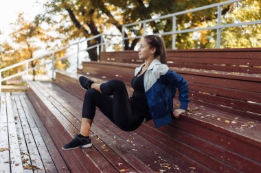 Sıska bir kadın ahşap tezgahlardan eller için ters şınav çekiyor. Açık hava eğitimi