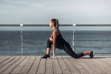 Eğitimden önce ısın. Mükemmel vücutlu zayıf genç bir kadın güneşli bir günde sahilde aerobik egzersizi yapıyor..