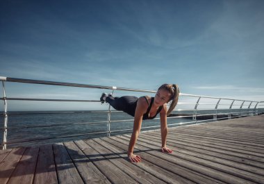 Eğitimden önce ısın. Mükemmel vücutlu zayıf genç bir kadın güneşli bir günde sahilde aerobik egzersizi yapıyor..