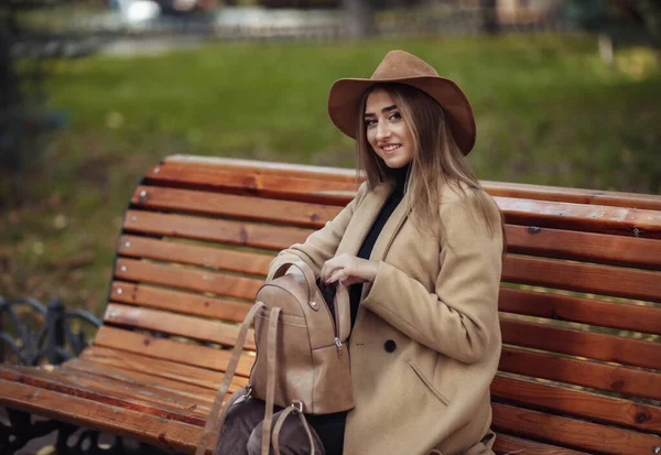 穿着秋装的年轻漂亮女子坐在城市公园的长椅上 穿着时髦外套和毛毡帽的女人 秋天的时间 — 图库照片