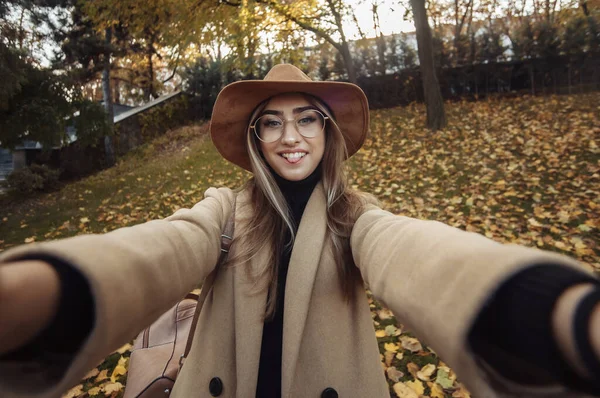 Selfie portrait of a funny young woman on the background of fallen leaves in the park. Autumn time