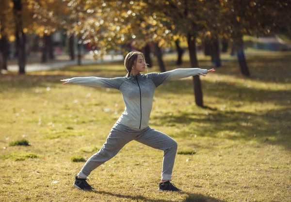 Genç sporcu kadın sonbahar parkında yoga yapıyor.