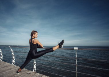 Spor kıyafetli zayıf bir kadın güneşli bir günde kumsalda bacak egzersizi yapıyor.