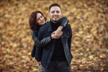 Parkta düşen sonbahar yapraklarının bulanık arka planında birbirine sarılan genç sevgililerin portresi..