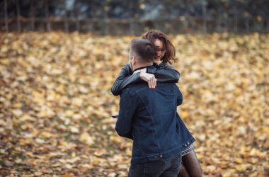 Genç aşıklar parkta düşen sonbahar yapraklarının bulanık arka planında birbirine sarılıyor. Romantik, aşk konsepti