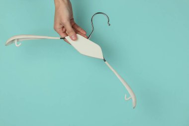 Kadın eli, mavi pastel arka planda elbise askısı tutuyor. Minimalist moda konsepti. Stüdyo çekimi. Üst görünüm